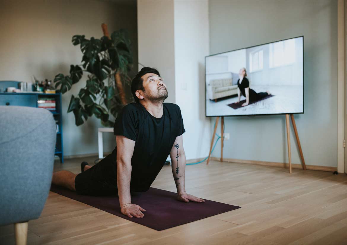 Hombre practicando yoga en el suelo junto a la televisión