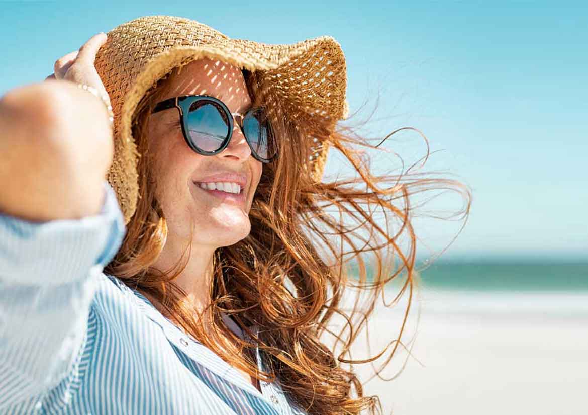 Mujer con gafas de sol sentada al sol sujetando su sombrero