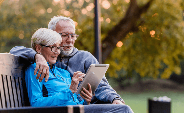 Older couple sitting together in park looking at iPad