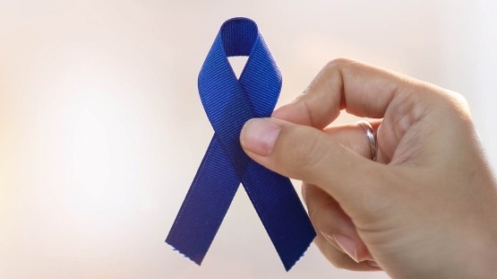 Una mano que sostiene una cinta azul oscuro para conmemorar el Mes de la Concientización sobre el Cáncer Colorrectal