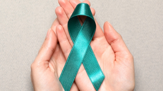 Hand holding teal ribbon to support cervical cancer awarenss month