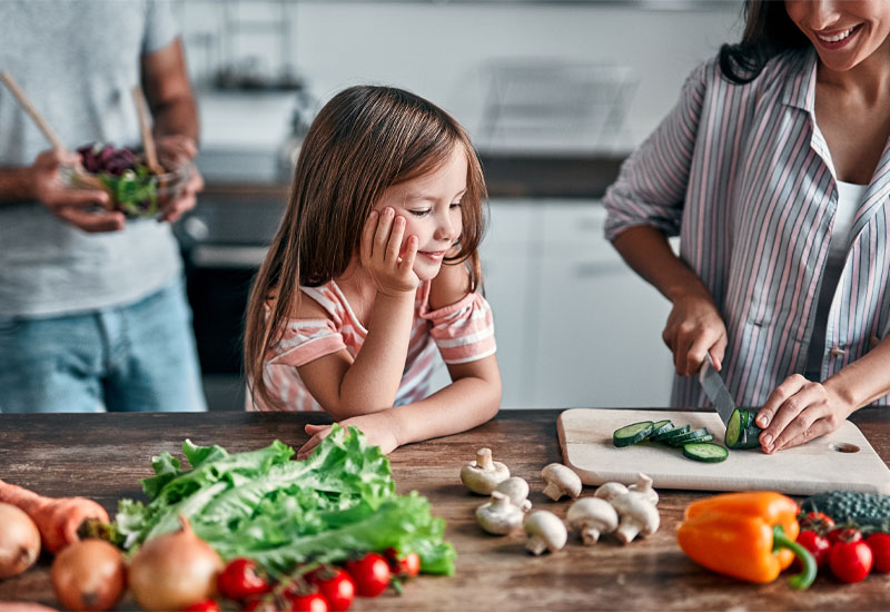 Mom cutting cucumbers for daughter in kitchen