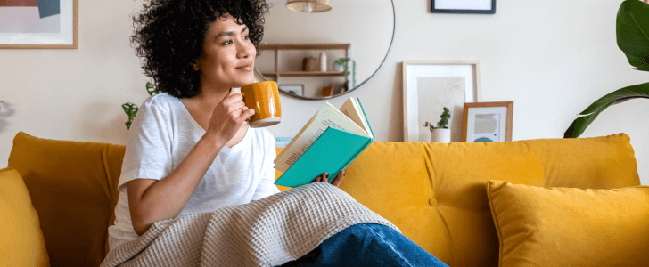 Woman sitting in living room holding a book and cup of coffee