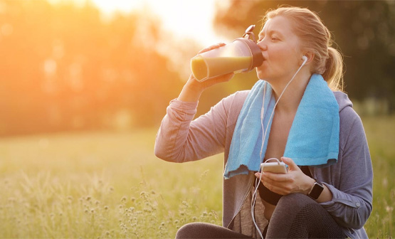 Mujer con auriculares que está sentada sobre el césped mientras bebe una botella de agua