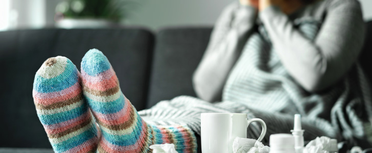 Woman sitting on sofa sneezing into tissue