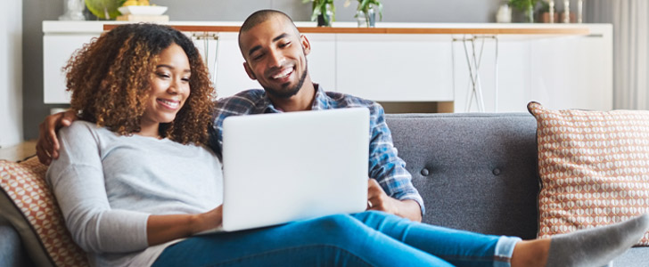 Couple sitting together on couch scrolling through laptop