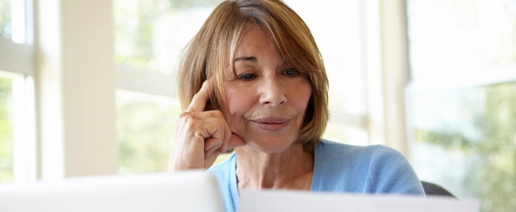 Older woman thinking while scrolling on laptop