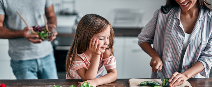 Mother cutting vegetables for daughter in kitchen