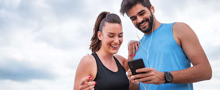 Smiling man and woman viewing smartphone in workout clothes