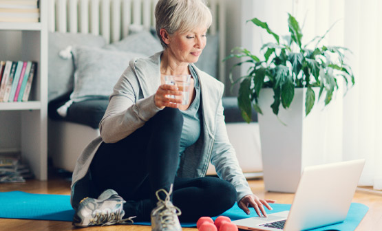 Mujer mayor viendo una computadora portátil mientras hace ejercicio con pesas